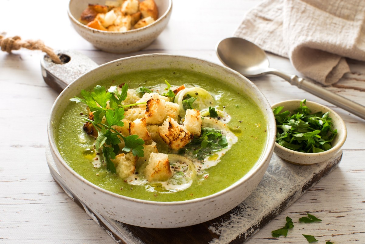 Eine SchÃ¼ssel Zucchini-Spinat-Suppe mit CroÃ»tons, Lauch, Schmand und KrÃ¤utern.