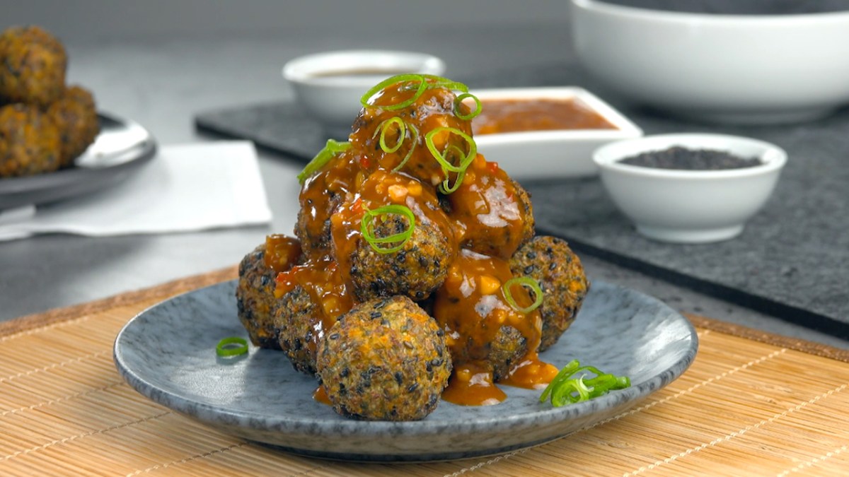 Eine Pyramide aus frittierten GemÃ¼sebÃ¤llchen mit Spitzkohl und schwarzen Sesamauf einem Teller.