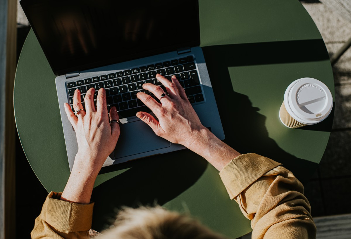 Eine Frau arbeitet draußen an ihrem Laptop. Neben dem PC steht ein Kaffee to go.