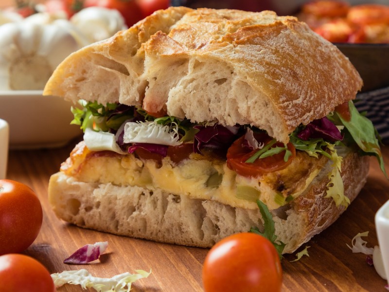 Frittata-Sandwich mit Salat, Tomate und Spinat, drumherum frische Zutaten, Nahaufnahme.