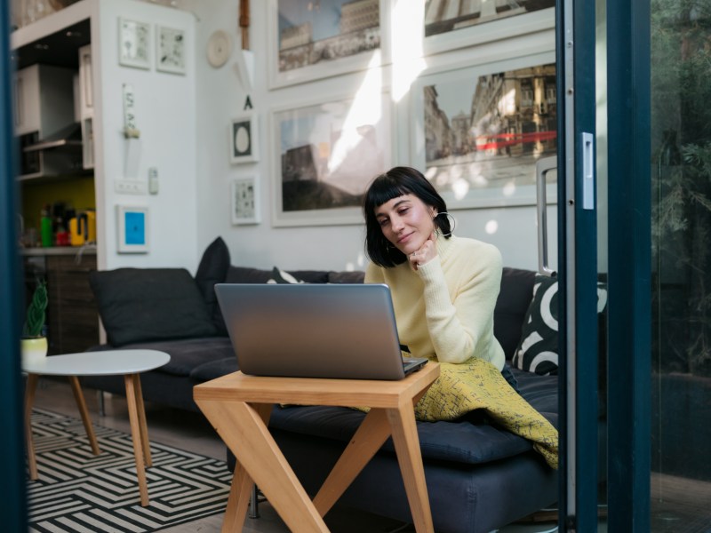 Junge Frau arbeitet bequem von ihrer Wohnung aus mit einem Laptop.