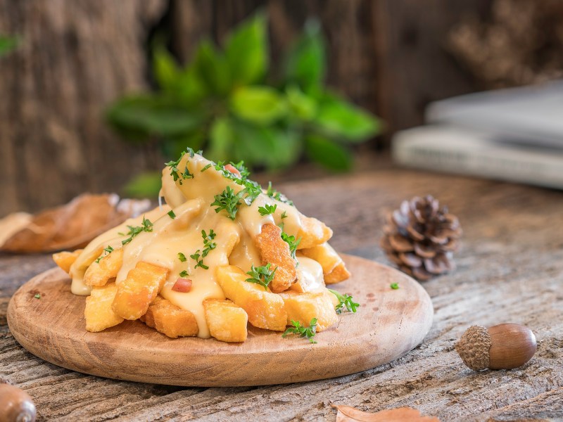 KÃ¤se-Pommes auf einem Brett, mit Petersilie bestreut.