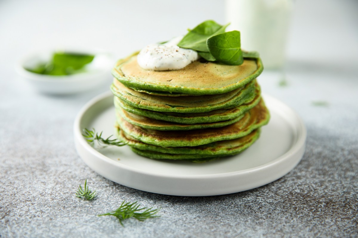 Vegane Spinat-Pancakes mit Sour Cream gestapelt auf einem Teller.