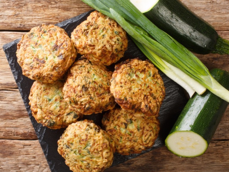 Mehrere Zucchini-BÃ¤llchen in der Draufsicht. Daneben liegen Zucchini und FrÃ¼hlingszwiebeln.