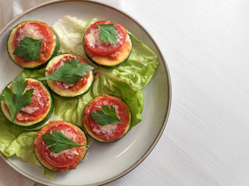 Zucchini-Bruschetta-HÃ¤ppchen mit Parmesan und Tomate auf einem Teller, Draufsicht.