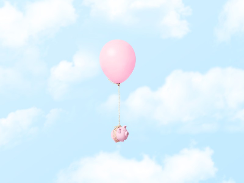 Ein einzelnes rosa Sparschwein, das an einem Ballon mit einem Seil befestigt ist, das durch die Wolken schwebt.
