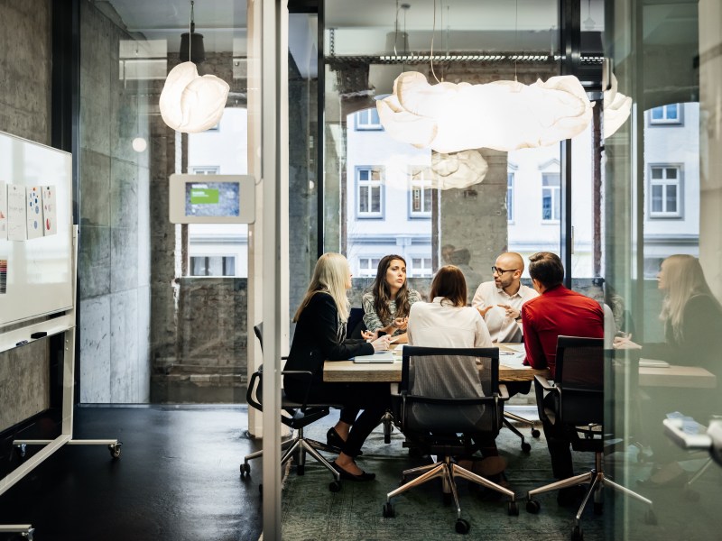 Eine Gruppe von Personen sitzt während eines Meetings in einem hellen, modernen Büro an einem Tisch.