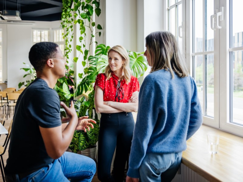 Drei Arbeitskollegen stehen an einem Fenster und unterhalten sich.