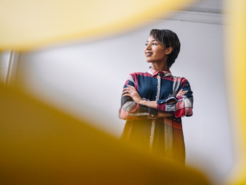 Eine Frau steht im Büro mit verschränkten Armen.