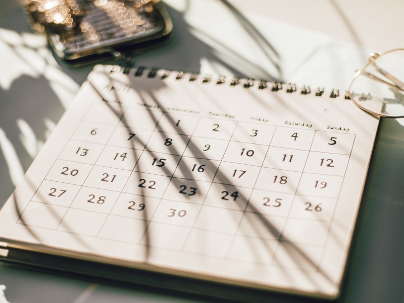 Kalender auf einem Tisch mit Blumen, Kaffeetasse und Notizbuch.