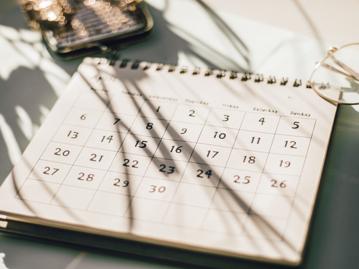 Kalender auf einem Tisch mit Blumen, Kaffeetasse und Notizbuch.