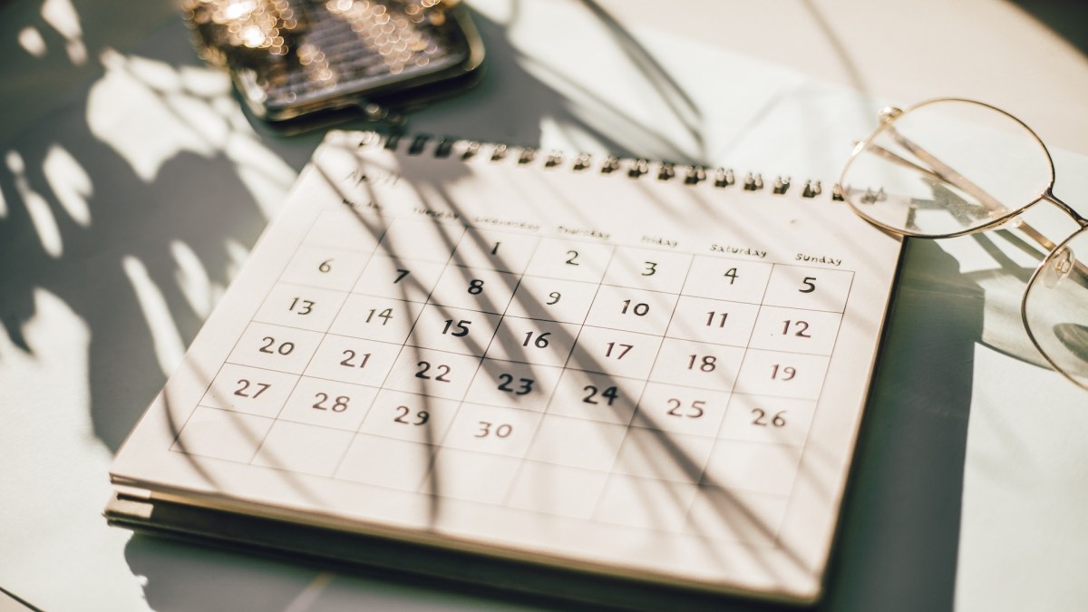 Kalender auf einem Tisch mit Blumen, Kaffeetasse und Notizbuch.