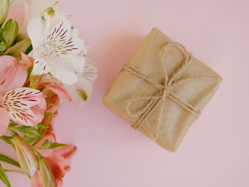Bunte rosa und weiße Alstroemeria-Blüten und Geschenkbox mit braunem Kraftpapier auf rosa Hintergrund.