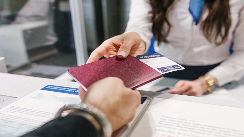 Eine Nahaufnahme eines Reisepasses und einer Bordkarte, die einer Flughafenmitarbeiterin ausgehändigt werden.