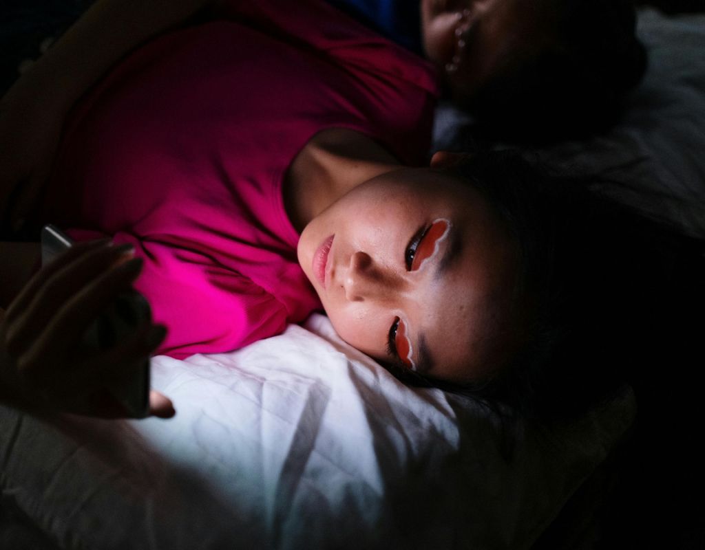 Frau liegt nachts im Bett mit Smartphone vor dem Gesicht