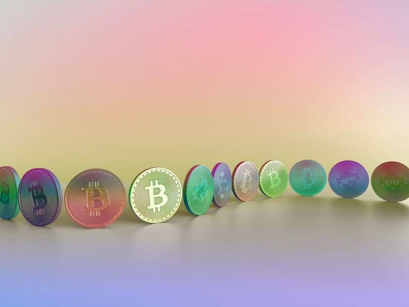 Ein pastellfarbenes, mehrfarbiges Bild einer zweifarbigen Münze mit Bitcoin-Symbol, angeordnet in einer Reihe oder Kette entlang einer Kurve vor einem mehrfarbigen Hintergrund.