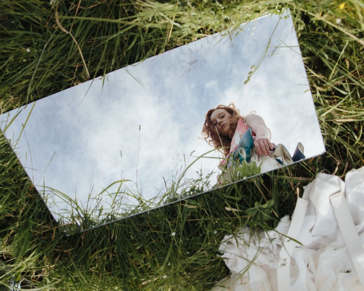 Ein Spiegel liegt im Gras und im Spiegelbild sieht man eine Frau, die hineinschaut.