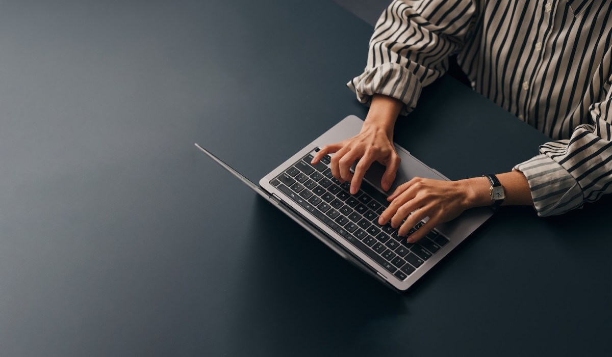 Eine Texterin, die an ihrem Schreibtisch sitzt und auf ihrem Laptop tippt.