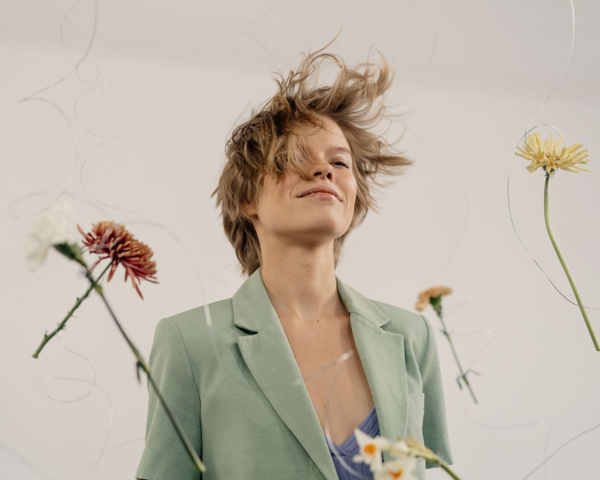 Frau mit Wind in den Haaren und Blumen, die an Fäden um sie herum schweben.