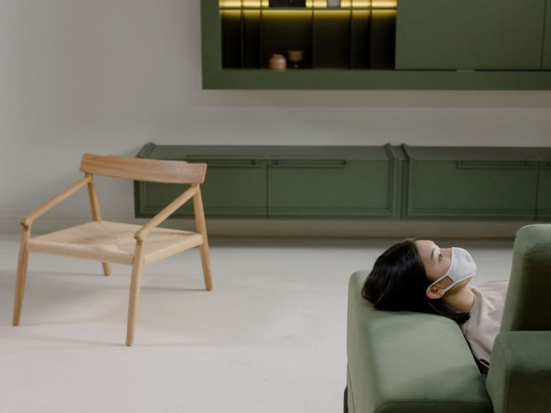 Frau liegt mit einer Maske vor dem Mund auf einem grünen Sofa