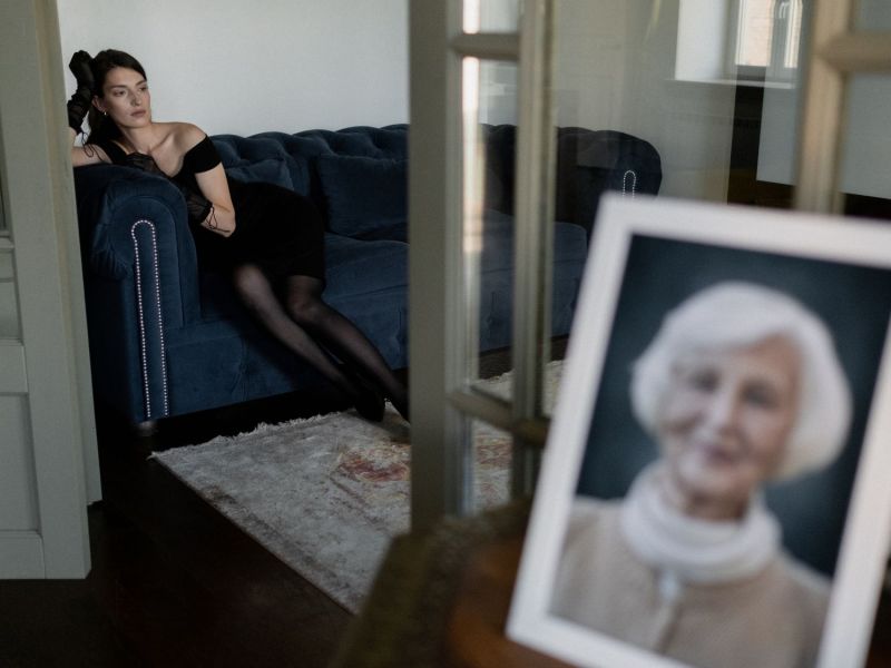 Frau sitzt auf dem Sofa und im Vordergrund steht ein Bild von ihrer Oma, verschwommen.