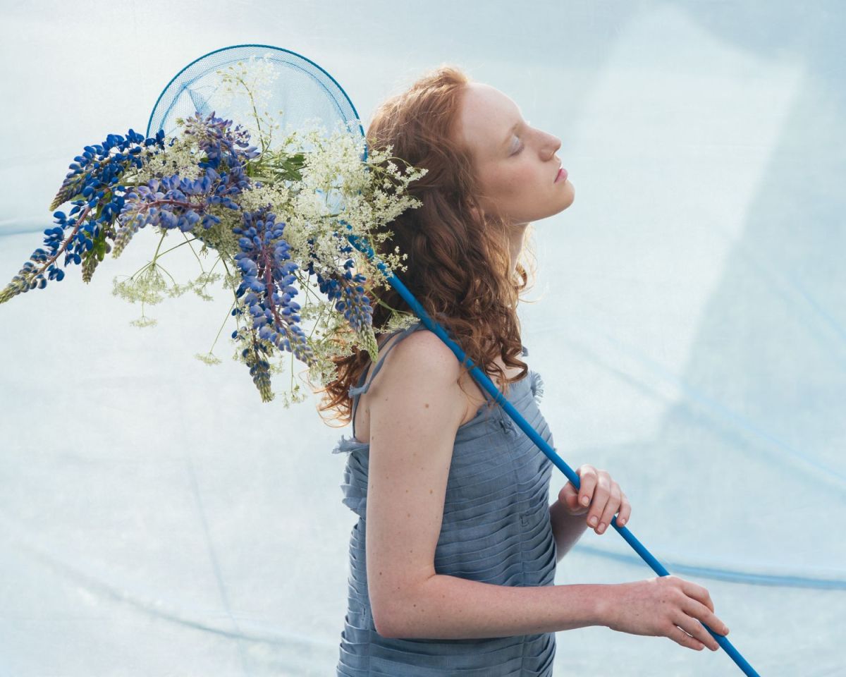 Frau mit einem Kescher voller Blumen über der Schulter