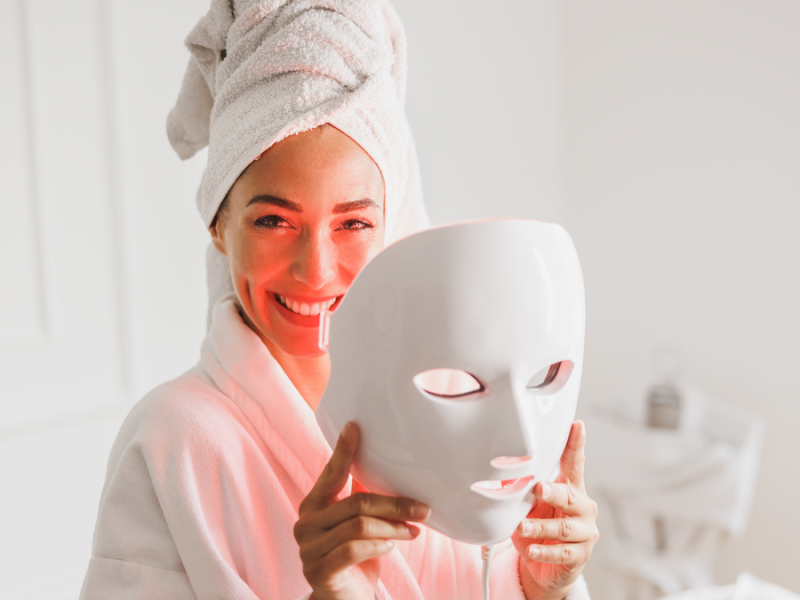 Frau lacht, hat ein Handtuch auf dem Kopf und hält eine LED Maske