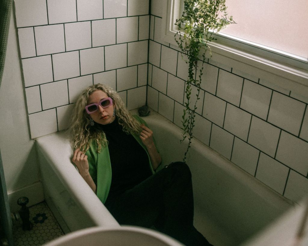 Frau sitzt in einer Badewanne, angekleidet.