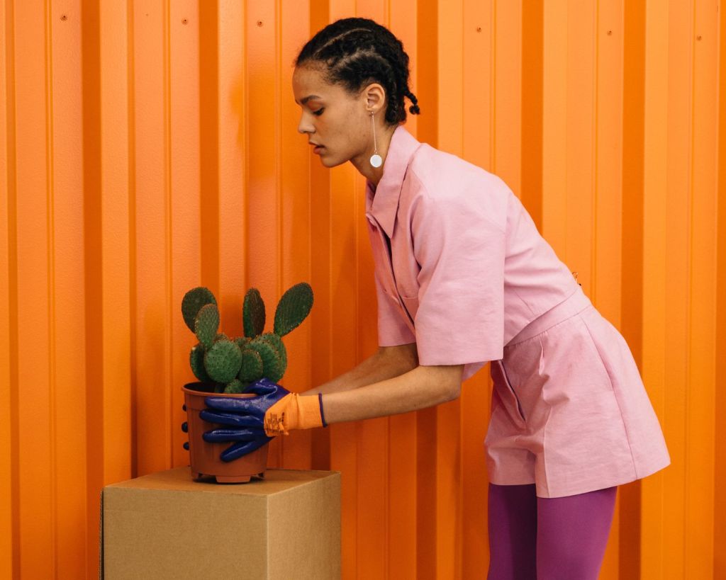 Frau kümmert sich vor einer orangefarbenen Wand um einen Kaktus.