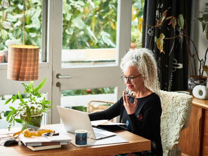 Grauhaarige Frau arbeitet zu Hause am Laptop.