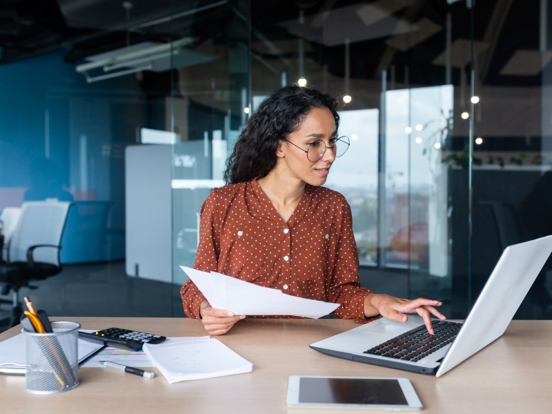 Geschäftsfrau mit Brille, die im Büro mit Dokumenten arbeitet.