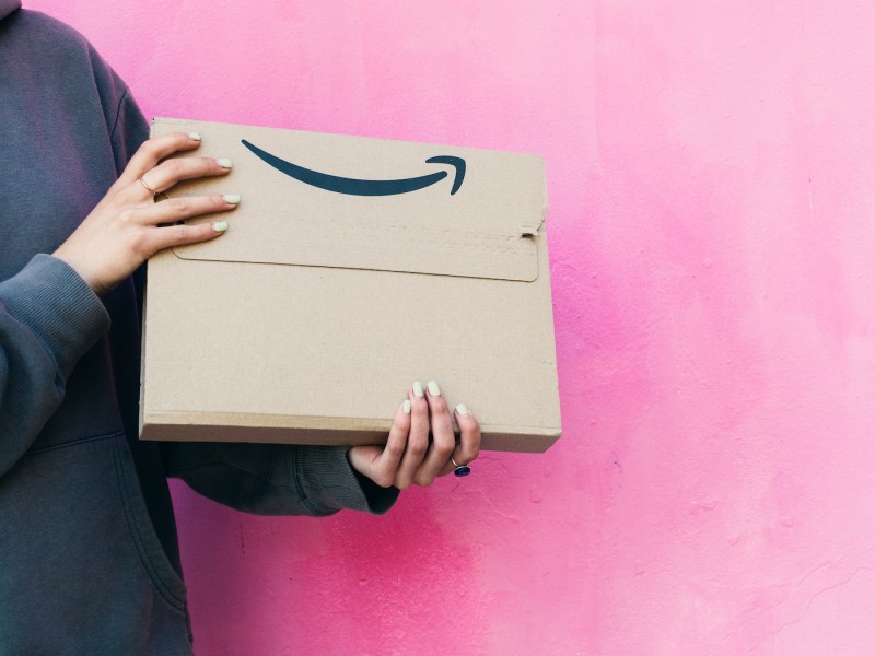 Körper einer jungen Frau, die ein Amazon-Paket in der Hand hält.