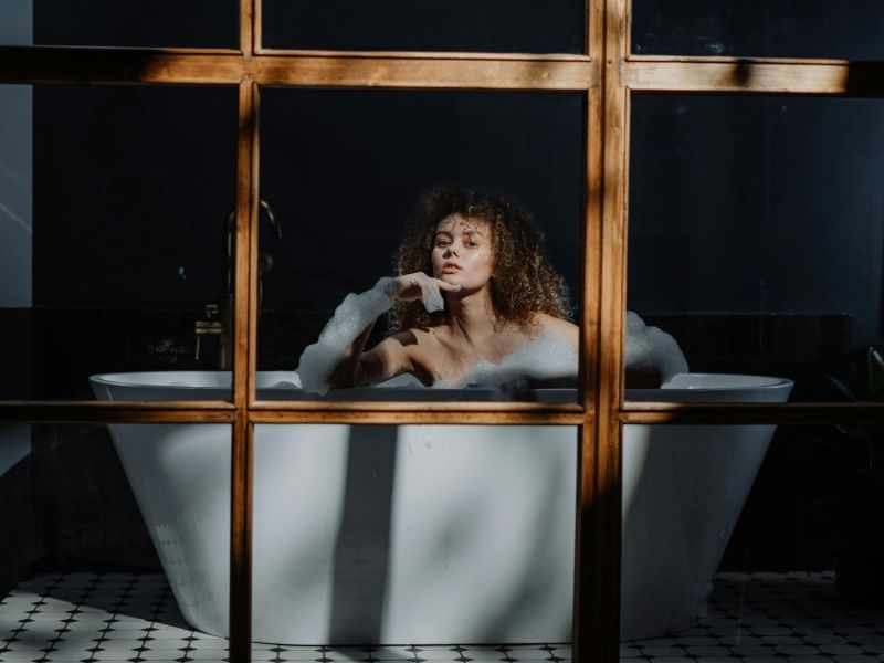 Frau sitzt in einer Badewanne und schaut in die Kamera.