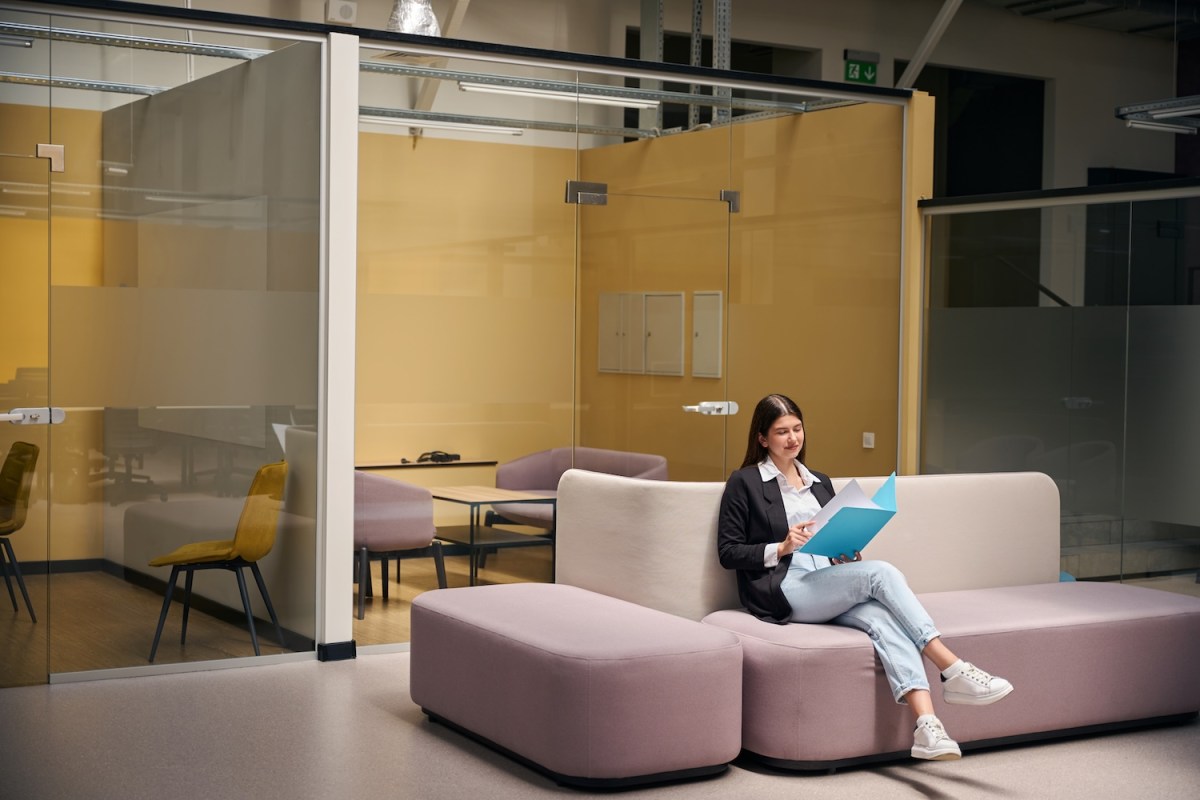 Frau in Jacke sitzt auf einem Sofa mit Dokumenten in einem blauen Ordner.