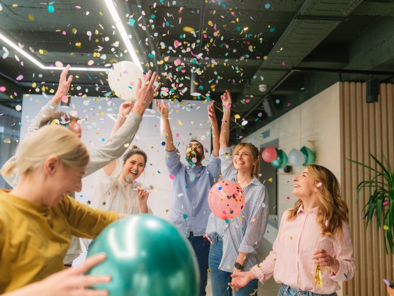 Foto einer Gruppe von Kollegen, die einen freudigen Anlass haben und gemeinsam an ihrem Arbeitsplatz feiern.