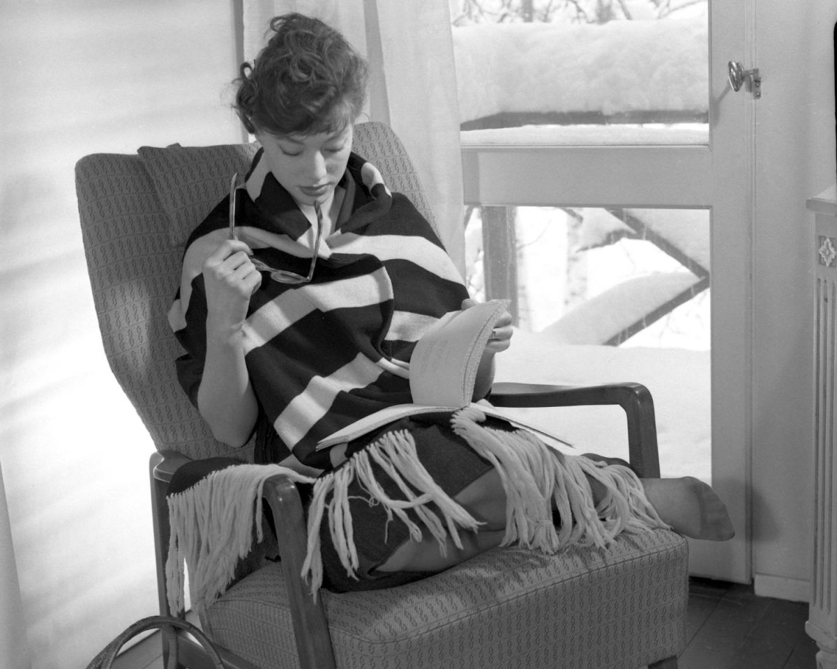 Frau aus den 1950er-Jahren liest auf einem Sessel.