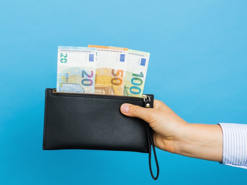 Weibliche Hände halten schwarze Brieftasche mit Euro-Banknoten auf blauem Hintergrund.