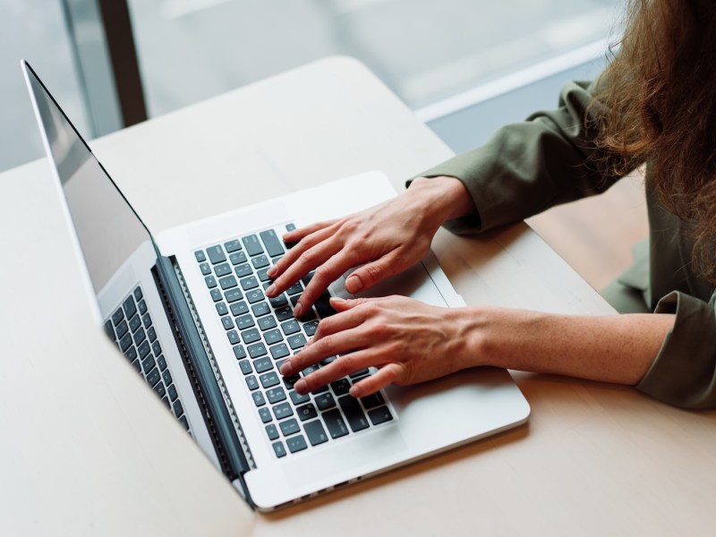Eine Nahaufnahme einer berufstätigen Frau, die an einem modernen Büroschreibtisch mit einem Laptop arbeitet. Ihre Hände tippen auf der Tastatur.