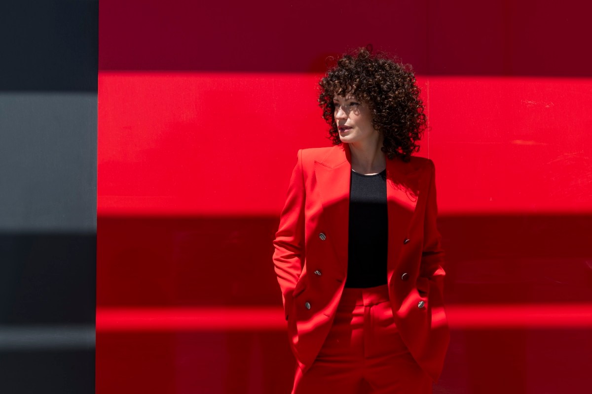 Selbstbewusste Geschäftsfrau mit Händen in den Taschen steht in der Nähe der roten Wand.