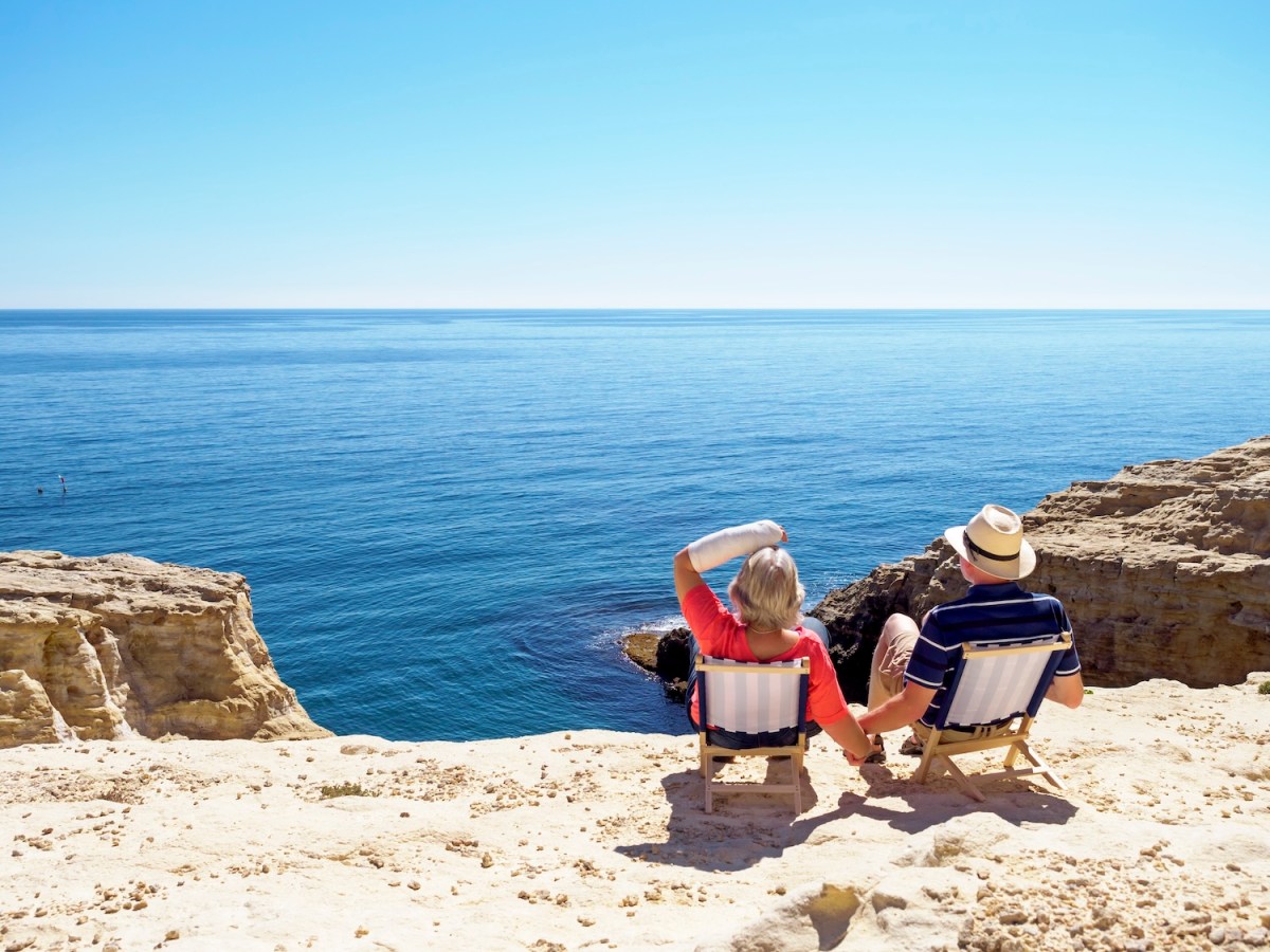 Rentner-Ehepaar sitzt auf Klappstühlen am Meer.