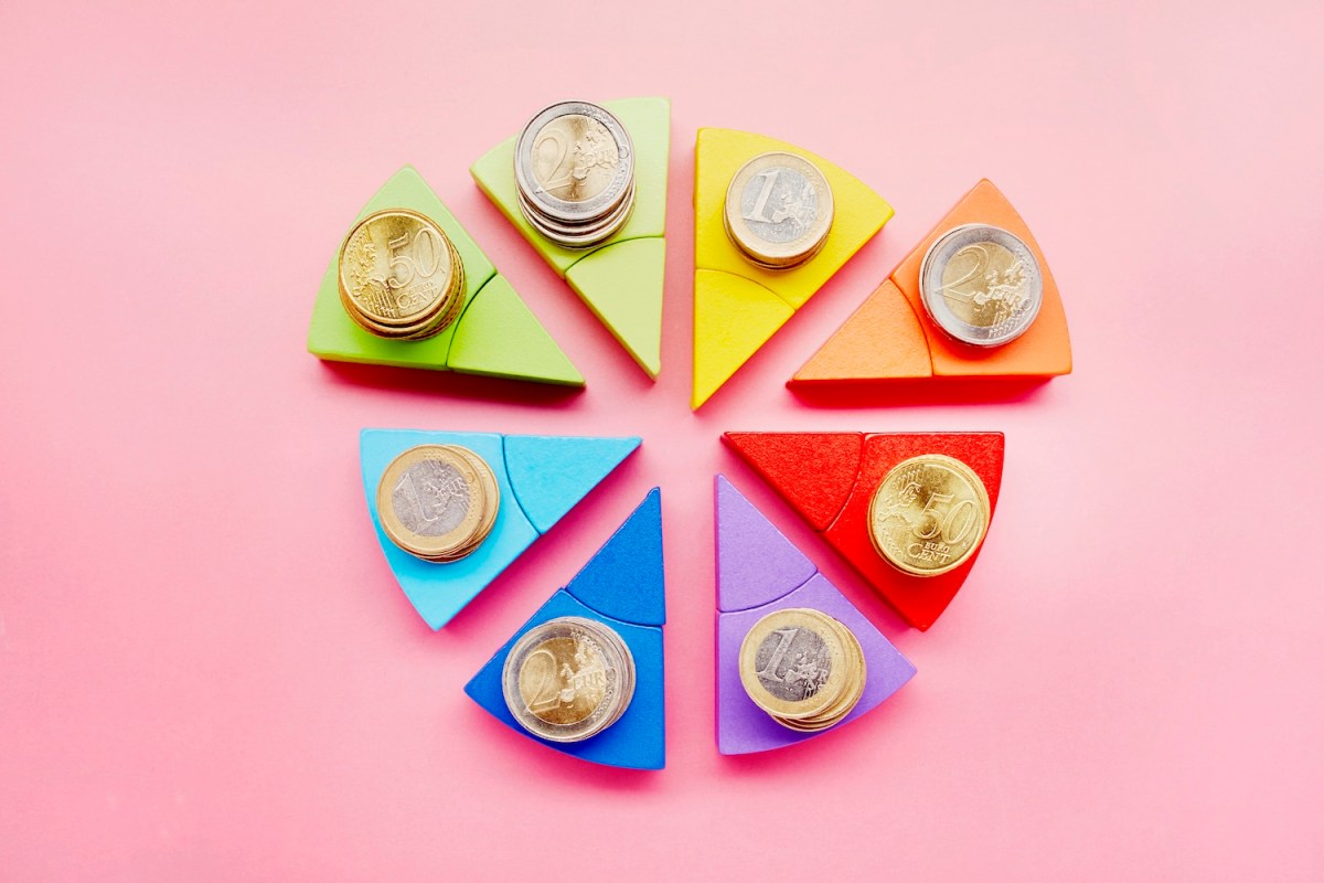 Kreisdiagramm aus bunten Bausteinen und Stapeln von Euro-Münzen auf rosa Hintergrund.