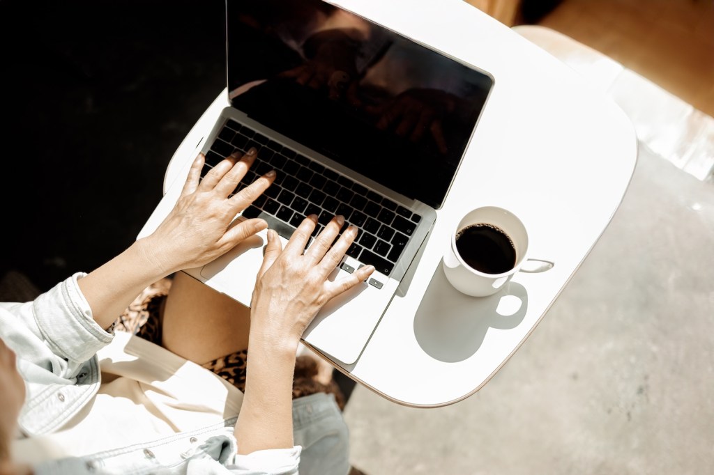 Eine reife Frau mittleren Alters arbeitet remote mit einem Laptop und Kaffee.