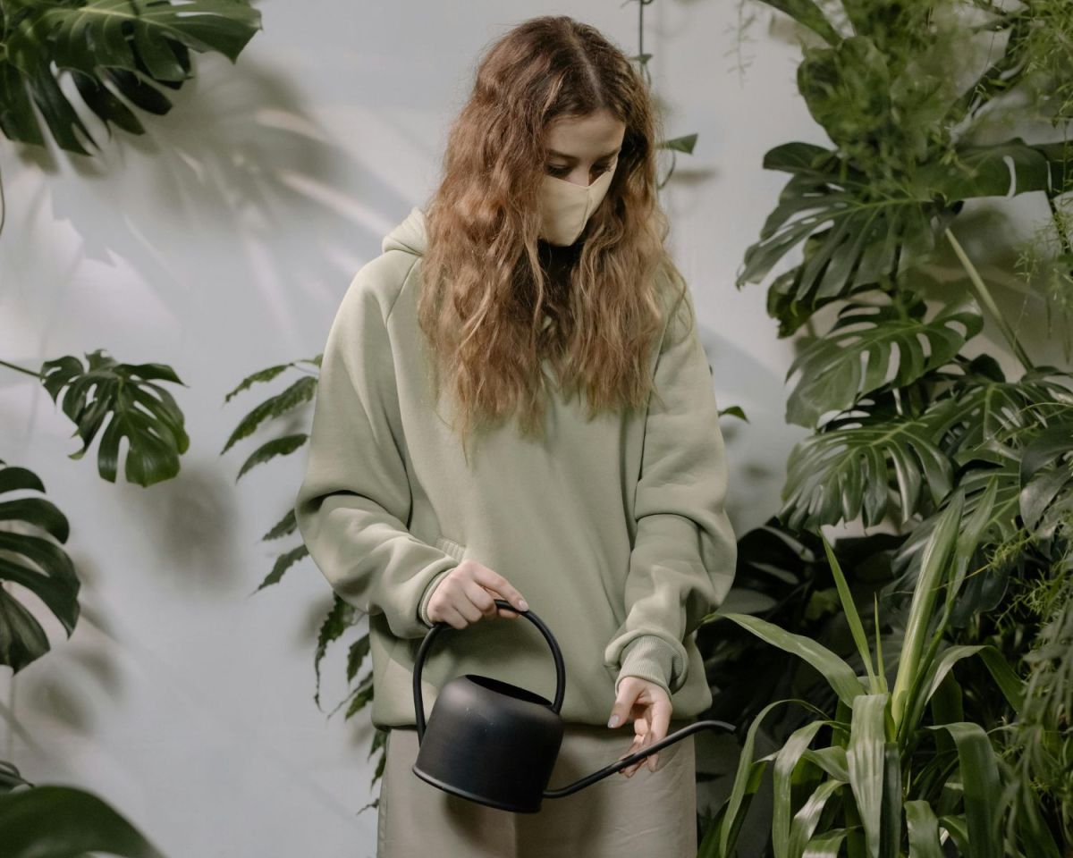 Frau mit einer Maske über dem Mund gießt Blumen.