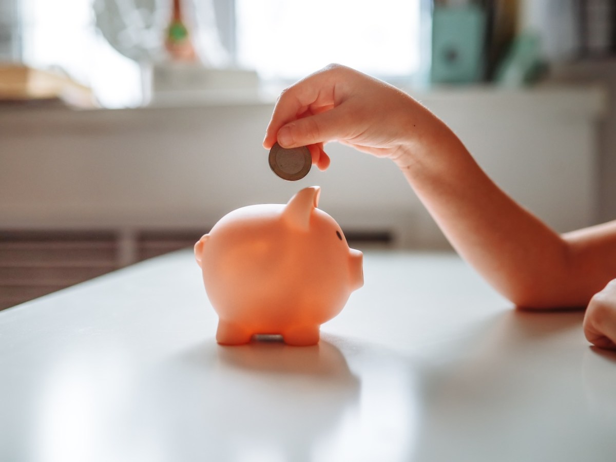 Mädchen wirft eine Münze in ein Sparschwein.