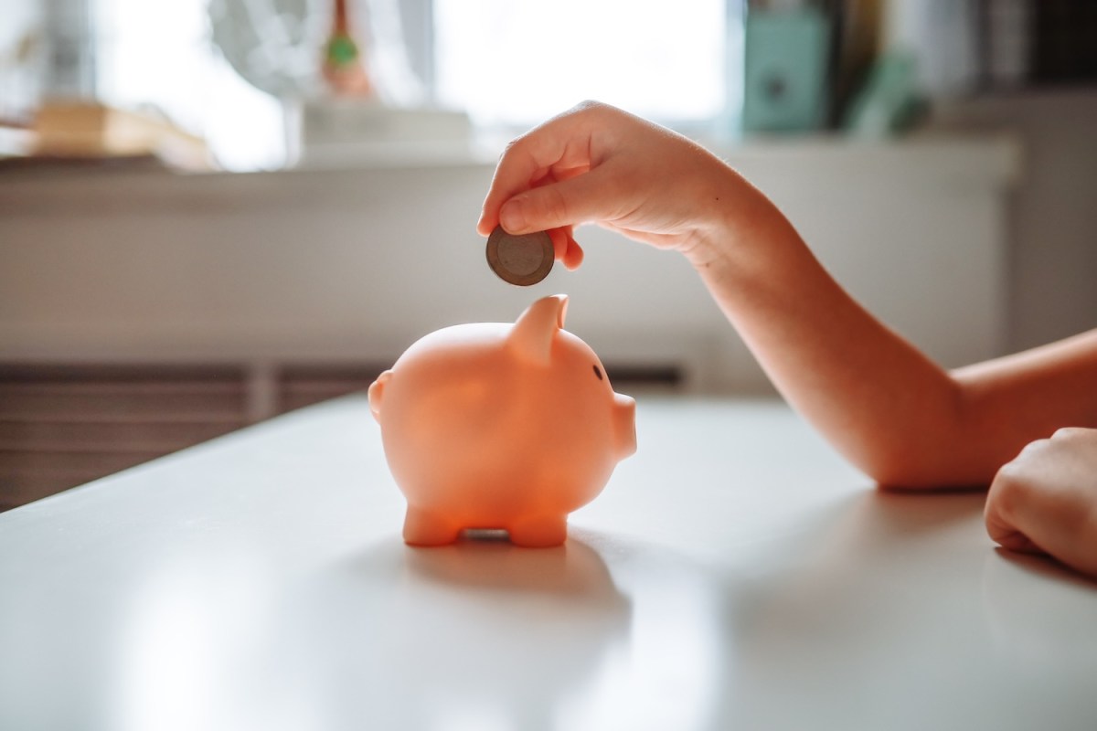 Mädchen wirft eine Münze in ein Sparschwein.