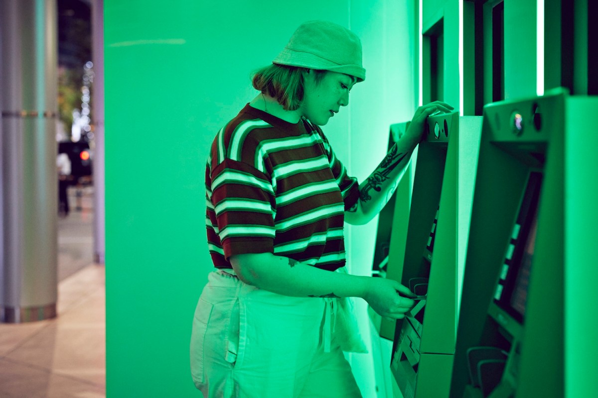 Junge Frau im gestreiften Shirt hebt Geld am Geldautomaten ab.