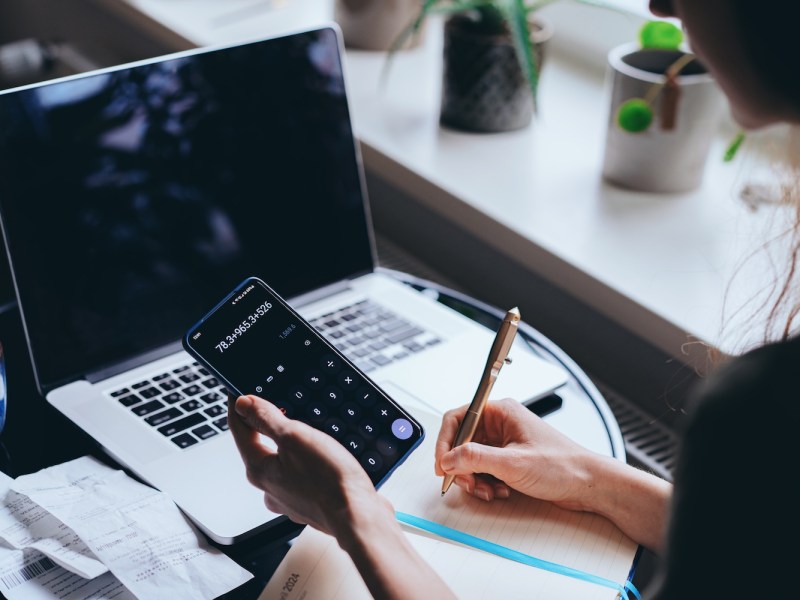 Nahaufnahme einer Frau, die einen Taschenrechner und einen Laptop zur Verwaltung ihrer Finanzen verwendet.