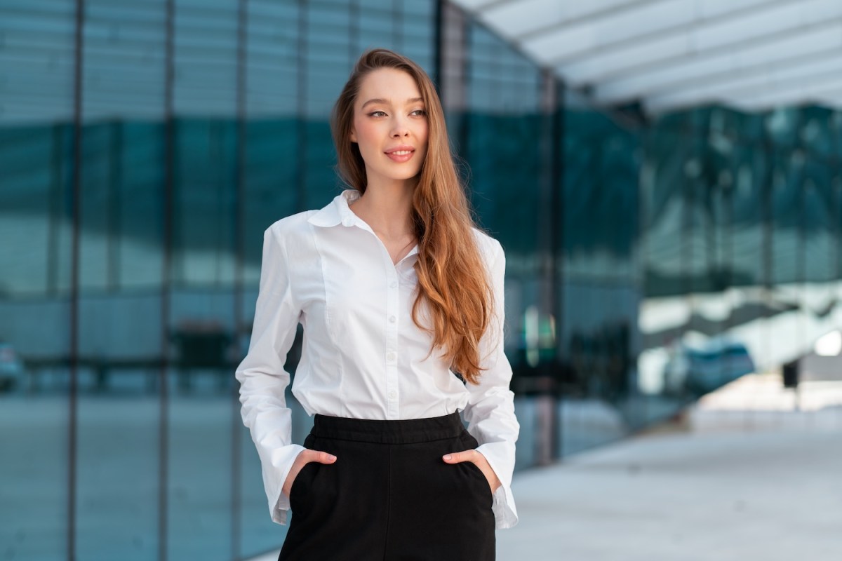Selbstbewusste Geschäftsfrau mit langen Haaren steht vor einem modernen Bürogebäude.