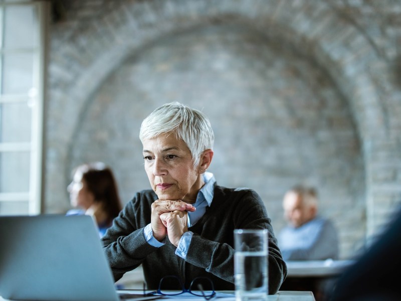 Eine ältere Dame mit grauen kurzen Haaren arbeitet in einem Büro.