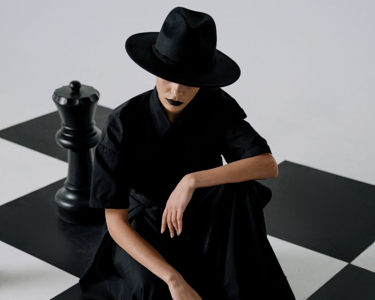 Frau mit schwarzem Hut auf einem Schachbrett-Muster-Boden.